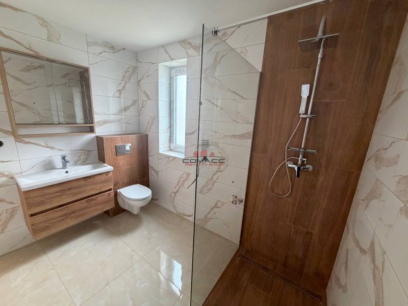 A bathroom with tiles and a wooden decor floor, with a shower and a toilet.