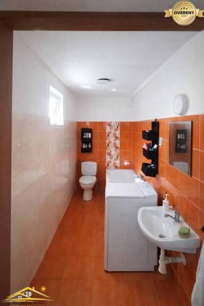 A bathroom in a family house with orange tiles, a washing machine, a sink, and a toilet.