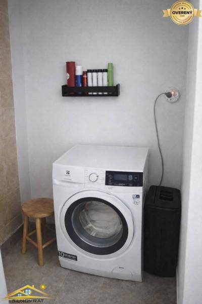 Washing machine in the laundry room of a family house, next to it are storage shelves and a chair.