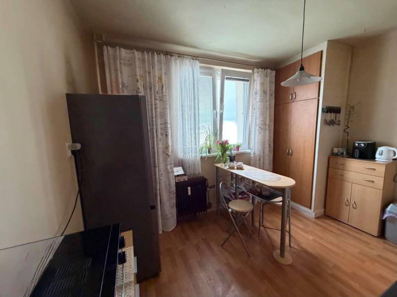 A kitchen in a 3-room apartment with a wooden decor floor, a table, and cabinets.