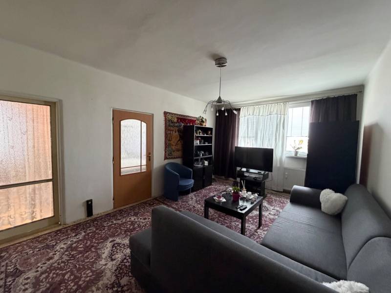 Living room in a three-room apartment with a dark sofa and a television on the carpet.