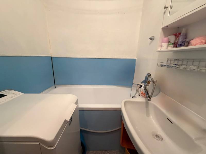 Bathroom in a 3-room apartment with a bathtub, sink, washing machine, and shelves.