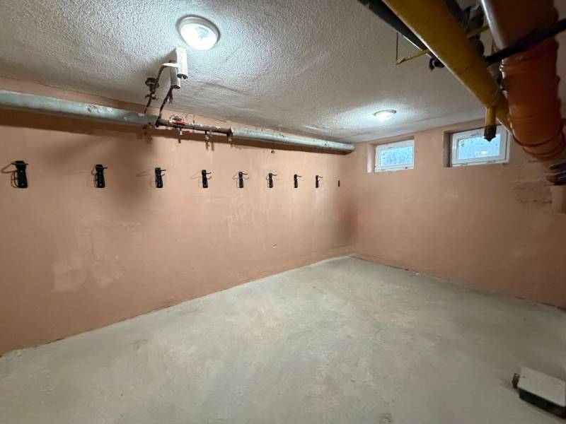 A small room in a 3-room apartment with hangers on the wall and pipes on the ceiling.