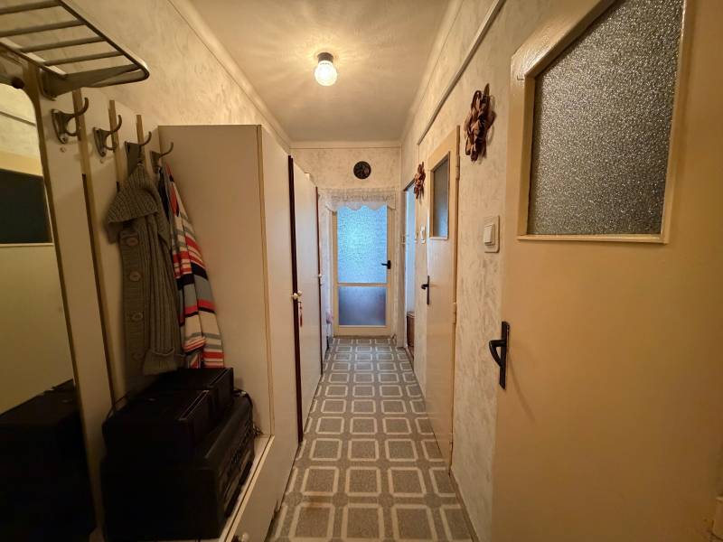 A narrow hallway in a 3-room apartment with a coat rack, a wardrobe, and a patterned floor.