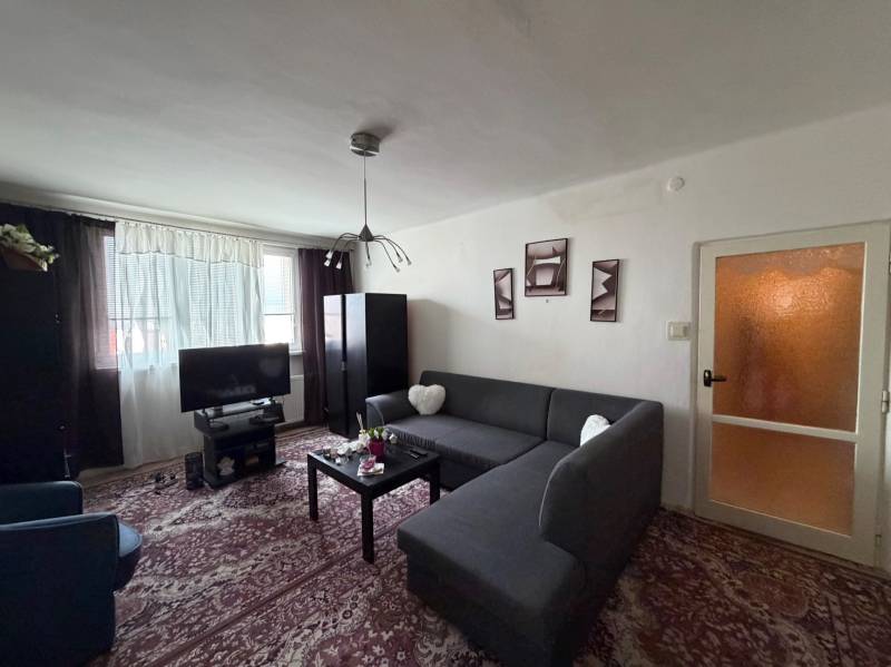 Living room in a three-room apartment with a corner sofa and dark furniture, floor with decor.