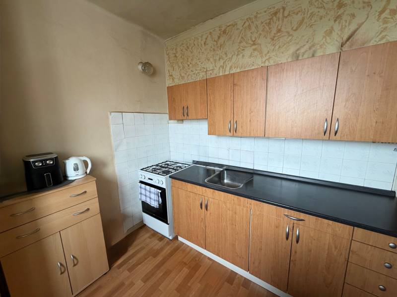 A kitchen with a gas stove, cabinets, and a wood-patterned floor in a 3-room apartment.