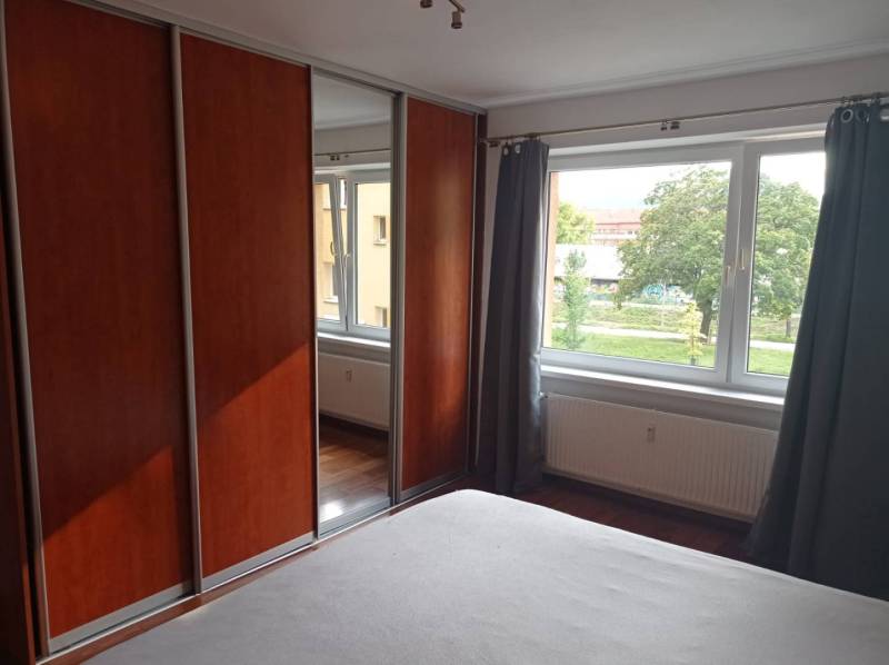 Bedroom in a 2-room apartment with a large wardrobe, window, and wooden decor flooring.