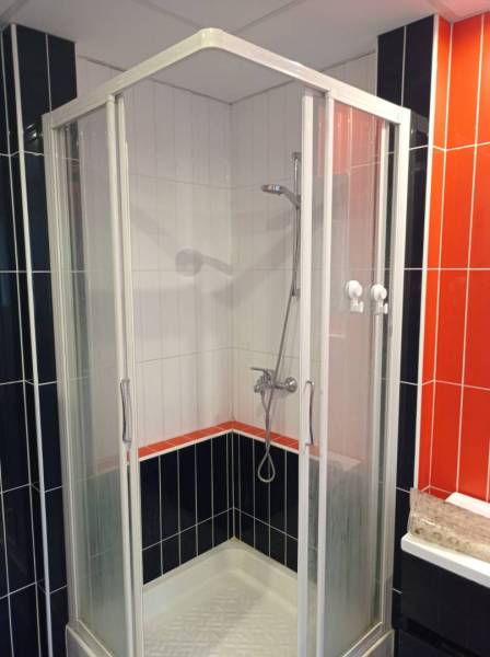 A shower corner with a combination of black, white, and orange tiles in a 2-room apartment.