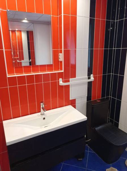 A bathroom with orange tiles, a mirror, and a sink in a 2-room apartment.