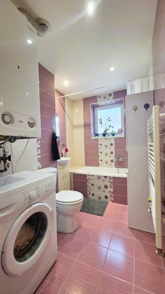Bathroom with a washing machine and a bathtub in a 2-room apartment, tiles in shades of pink.