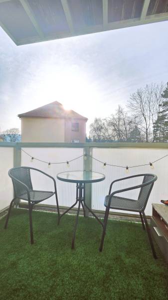A balcony with two chairs and a table, with green grass on the floor.