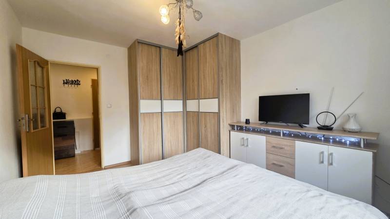 Bedroom in a two-room apartment with a wooden decor floor, built-in wardrobe, and dresser.