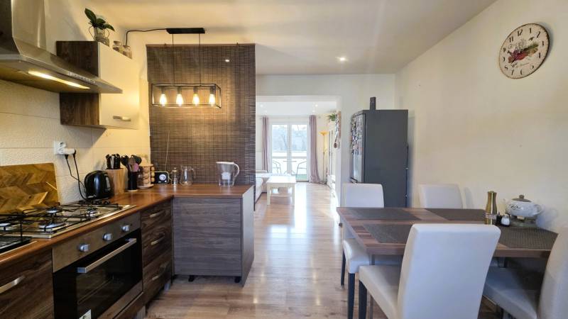 A kitchen in a 2-room apartment with a wooden decor floor, a dining table, and appliances.