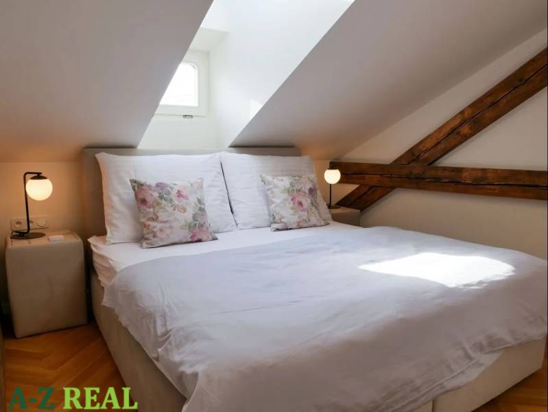 Attic bedroom in a 3-room apartment with exposed wooden beams and subdued lighting.