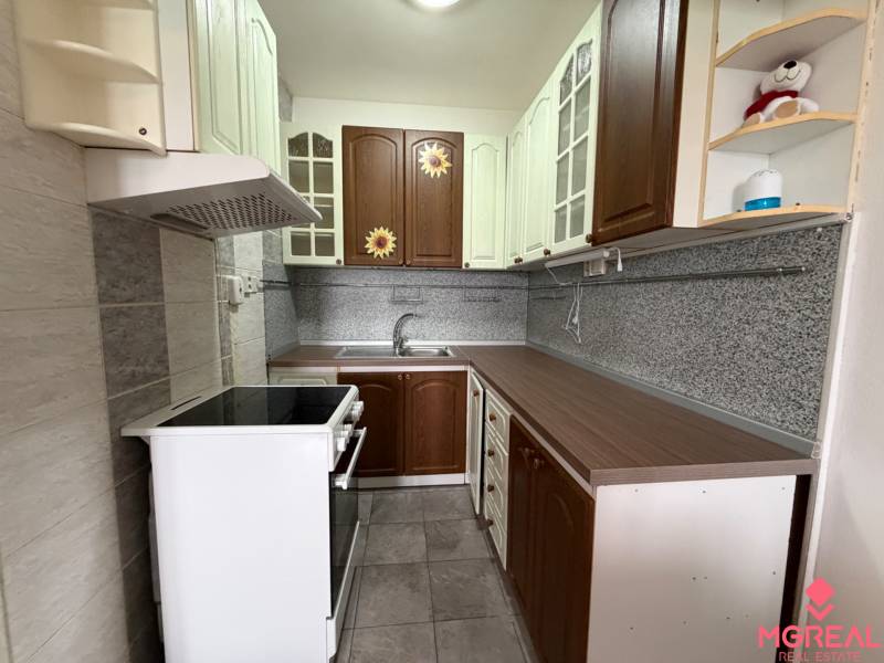 A kitchen in a 2-room apartment with a combination of wooden cabinets and gray tiles.