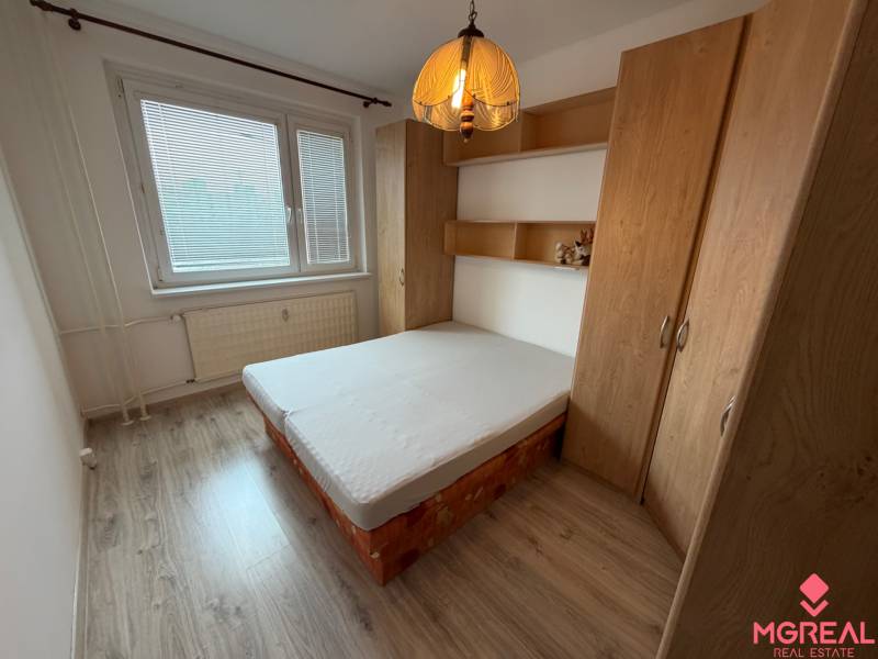 A bedroom in a two-room apartment with a wooden decor floor, a bed, and a built-in wardrobe.