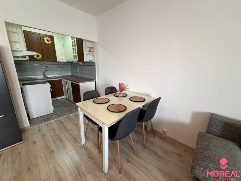 Dining room with kitchen, dining table, chairs, wooden decor flooring in a 2-room apartment.