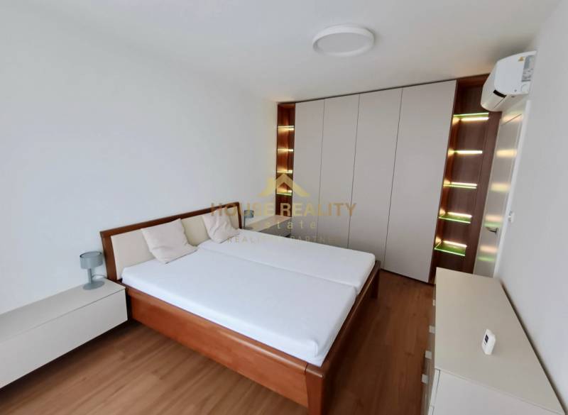 Bedroom in a two-room apartment with a wood-patterned floor and a built-in wardrobe.