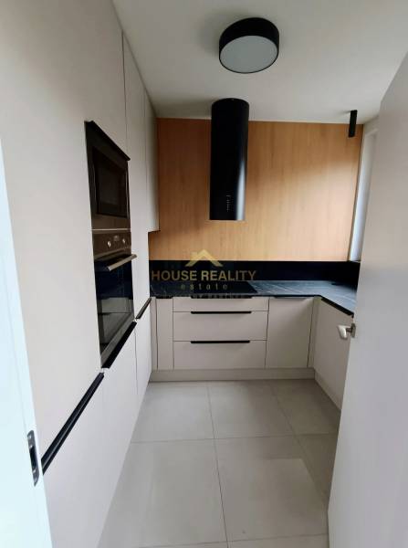 A kitchen in a 2-room apartment with white cabinets, a black extractor hood, and wooden decor.