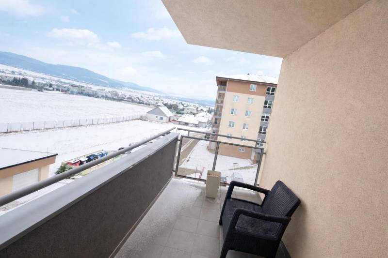 A balcony in a three-room apartment with a view of a snowy landscape and a parking lot.