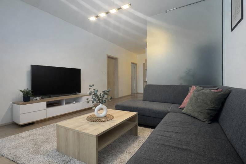 Living room in a 3-room apartment with a wooden decor floor, gray sofa, TV, and table.