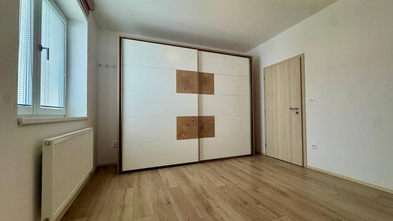 White built-in wardrobe, window with blinds, radiator, wooden decor flooring in a 3-room apartment.