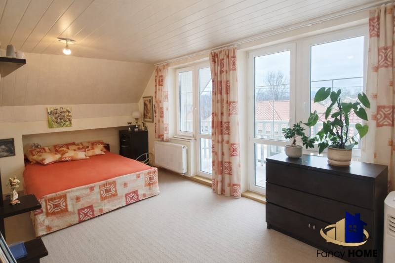 Bedroom in a family house with a bed, cabinet, large windows, and plants on the windowsill.