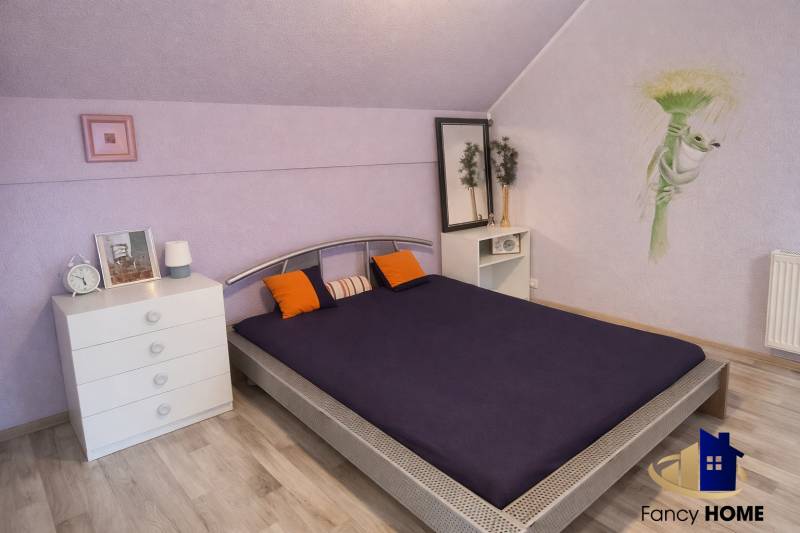 A bedroom in a family house with purple walls, a bed, a wooden decor floor, and decorations.