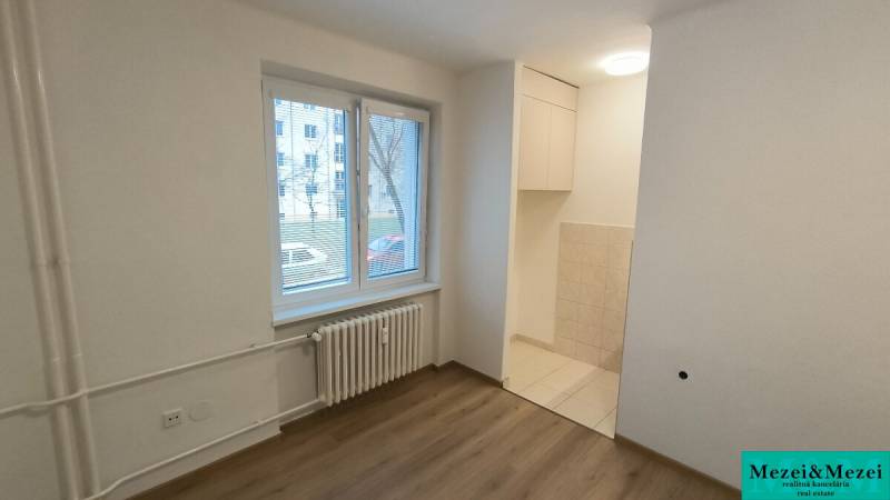 Studio apartment with a window, radiator, and floor with wood decor.