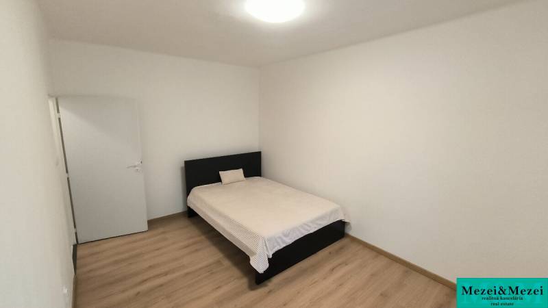 A bedroom in a studio apartment with a bed, white walls, and a floor with a wooden decor.