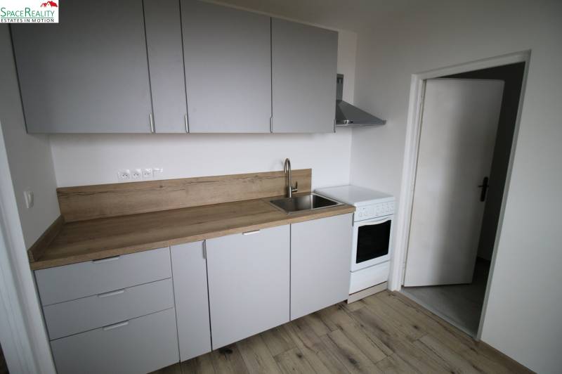 A kitchen in a 3-room apartment with a wooden decor floor and a simple kitchen unit.