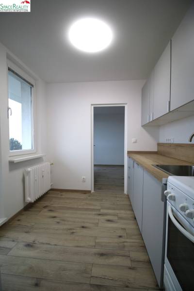 A kitchen in a 3-room apartment with a wooden decor floor, white cabinet, and stove.