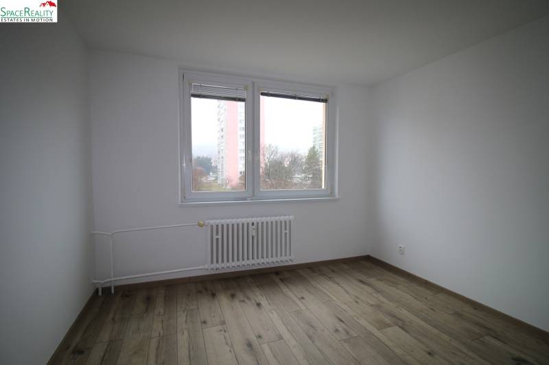 A room in a three-room apartment with a wooden decor floor and white walls.