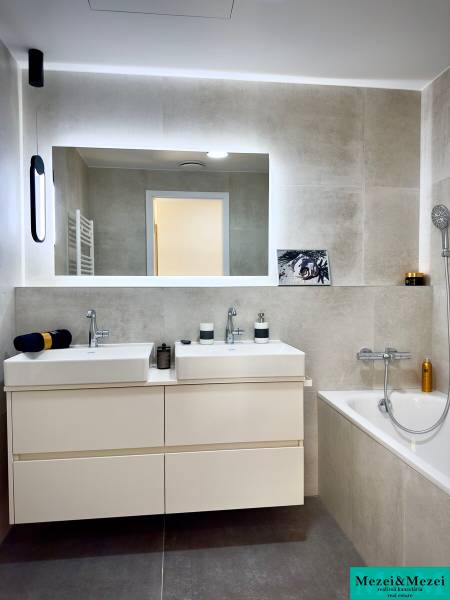 A bathroom in a 3-room apartment with two sinks, a bathtub, and a large mirror.