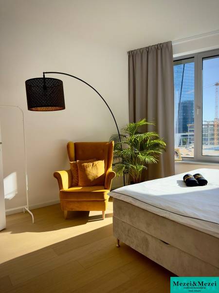 A bright bedroom in a three-room apartment with a striking chair, lamp, and plant.