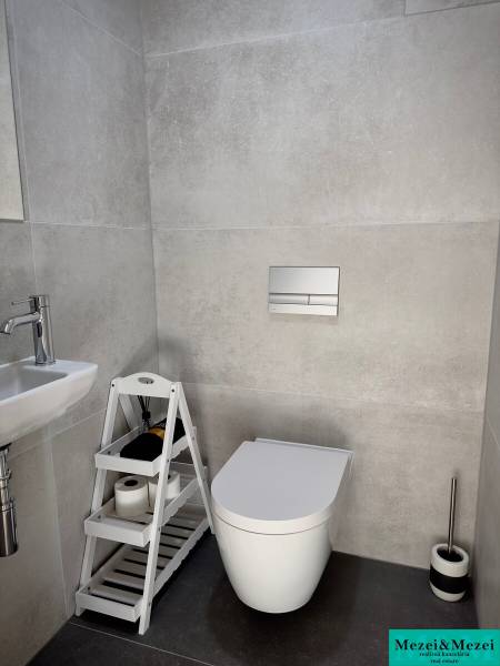Bathroom with wall-hung toilet, sink, and storage shelf in a 3-room apartment.