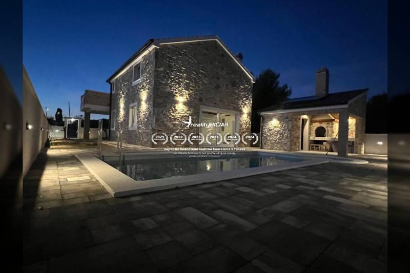 A family house in Vrsi on Vrsi Street with a stone facade and lighting by the pool.