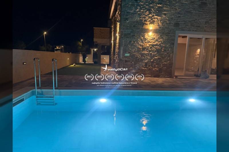 A family house in Vrsi with a pool and a stone facade illuminated by night lights.