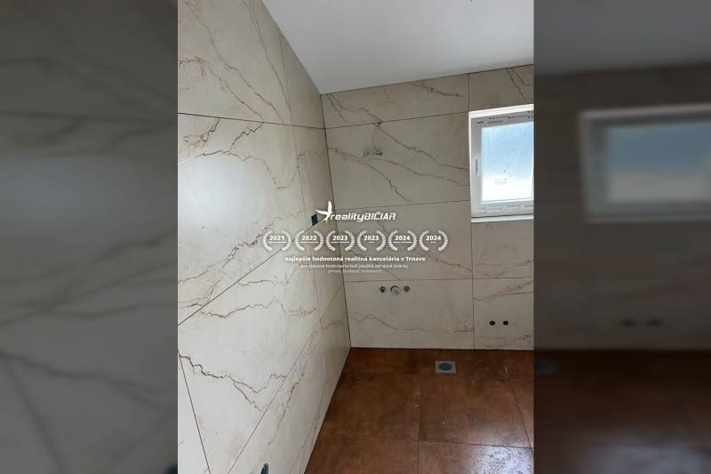 The bathroom in the family house has marble tiles and a small window.