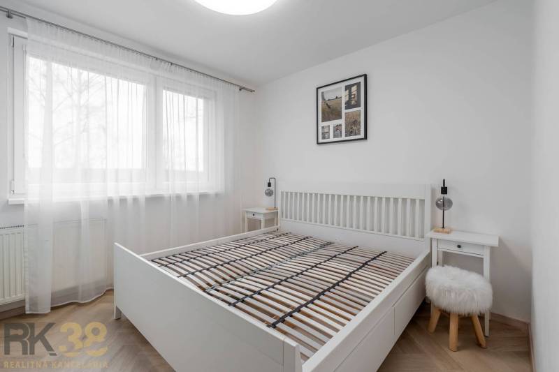 A bedroom with a white bed, nightstands, and a wooden decor floor in a 3-room apartment.