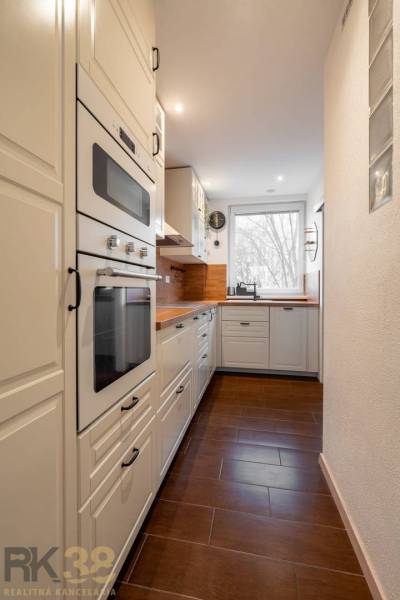 A kitchen in a 3-room apartment with white cabinets and a wooden decor floor.
