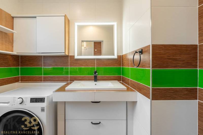 A bathroom in a 3-room apartment, with a sink, green tiles, and cabinets above the washing machine.