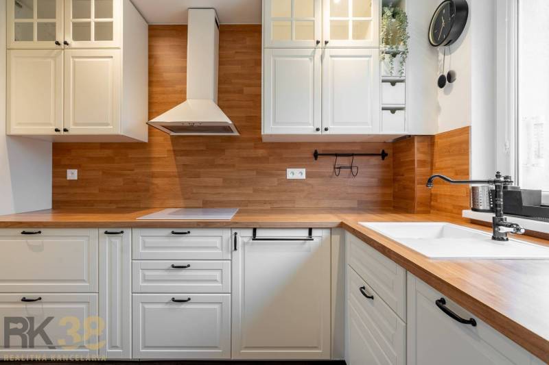 A kitchen in a 3-room apartment with a wooden decor floor and white cabinets.