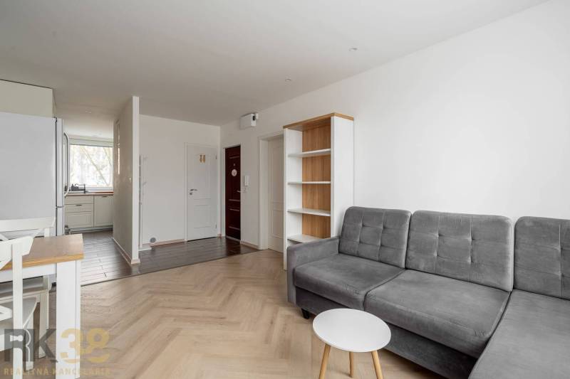 Living room in a three-room apartment with a wood-patterned floor and a gray sofa.