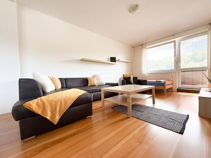 Living room of a two-room apartment with a corner sofa, a table, and a floor with a wooden decor.