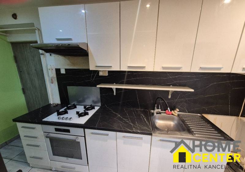 A kitchen in a 3-room apartment with an elegant white unit and black tiles.