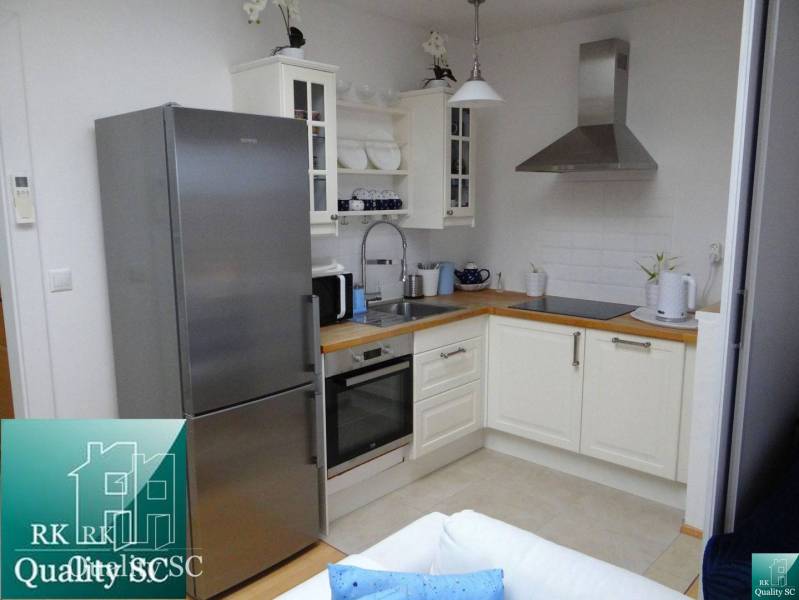 A kitchen in a studio apartment with modern equipment, stainless steel refrigerator, and white cabinets.