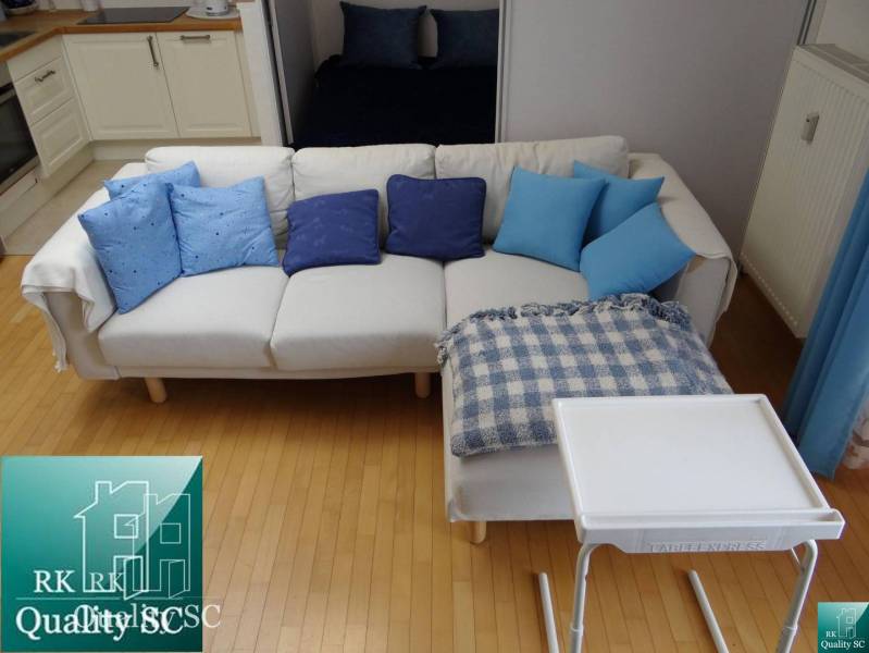 A one-bedroom apartment with a white sofa, blue cushions, and a wooden decor floor.