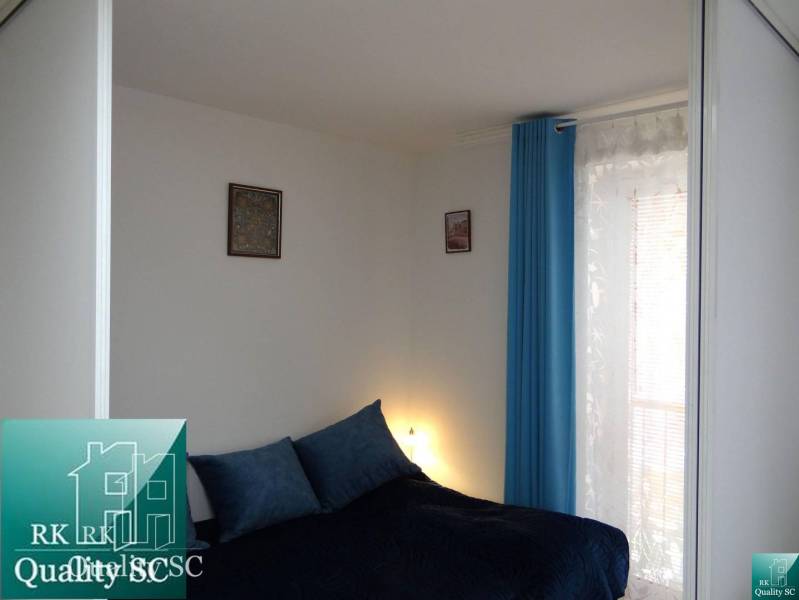 Bedroom in a studio apartment with blue curtains and decorative pillows on the bed.