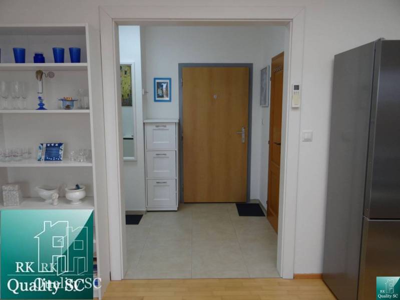 Interior of a 1-room apartment with a shelf, refrigerator, and wooden decor flooring.
